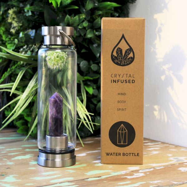 crystal infused glass bottle with packaging in front of a green bush