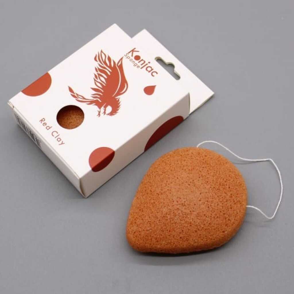 a reddish coloured teardrop konjac sponge infused with red clay, pictured with its packaging