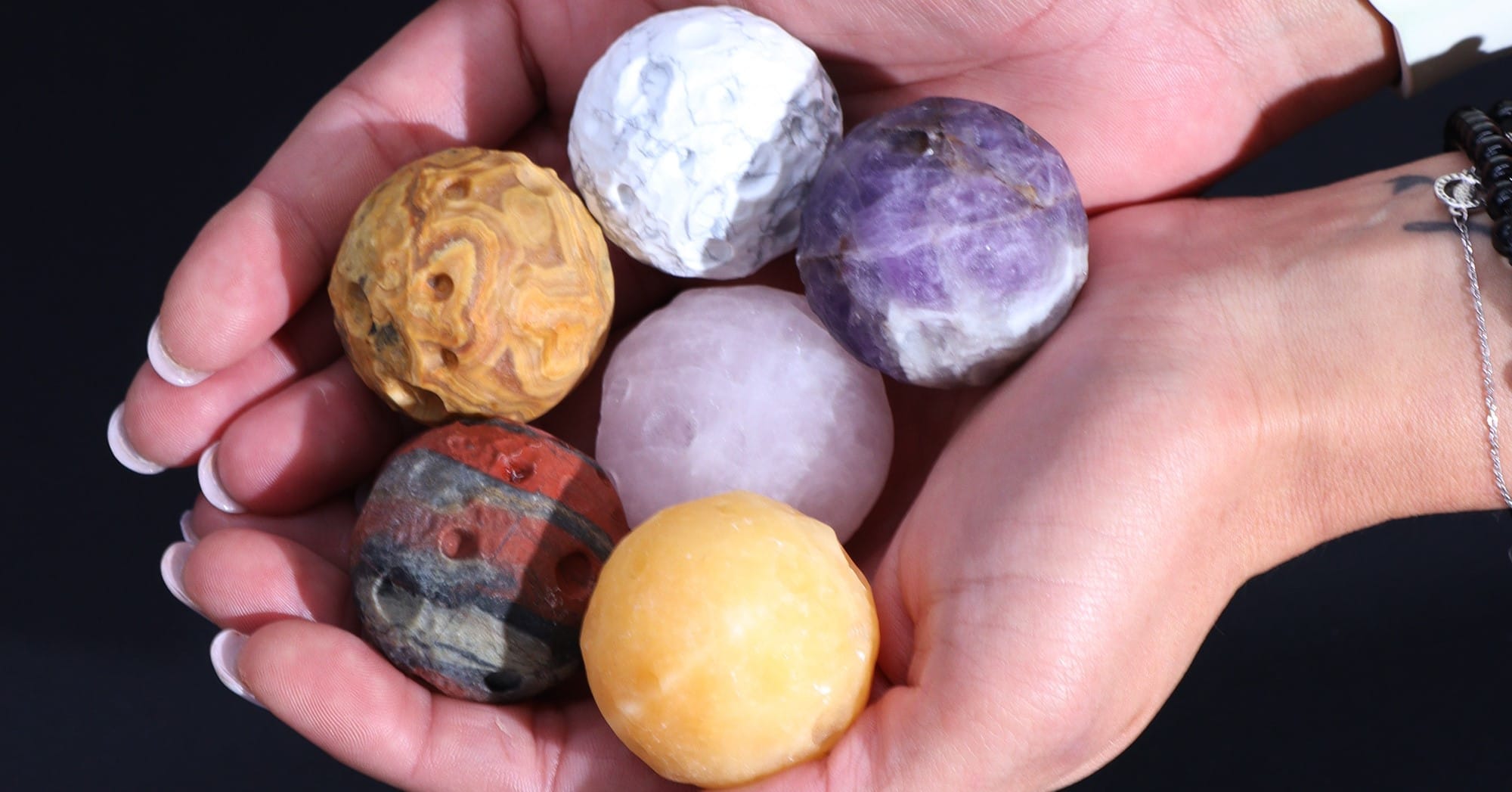 six various gemstone planets held in the palms of two hands