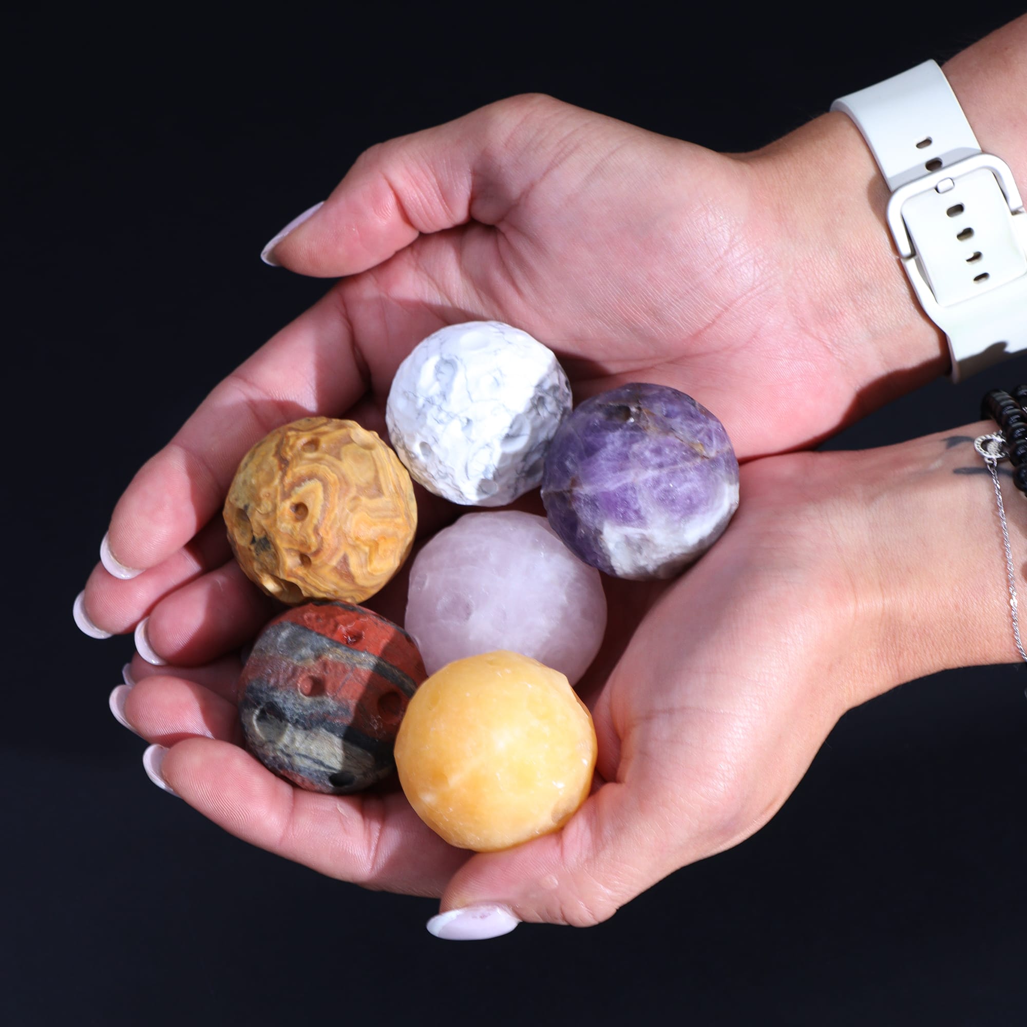 six various gemstone planets held in the palms of two hands