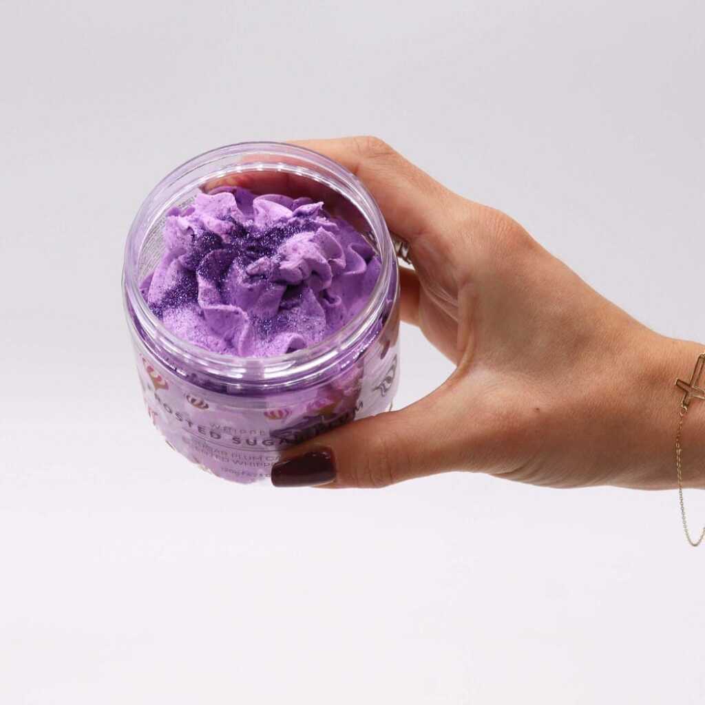 an open jar of Frosted Sugar Plum whipped soap, held between thumb and fingers
