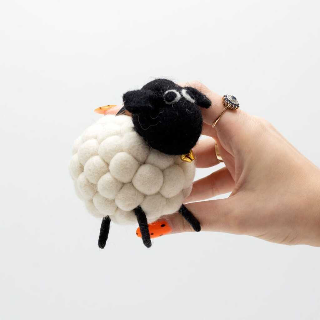 a little felt sheeps in white with a black head held in a hand