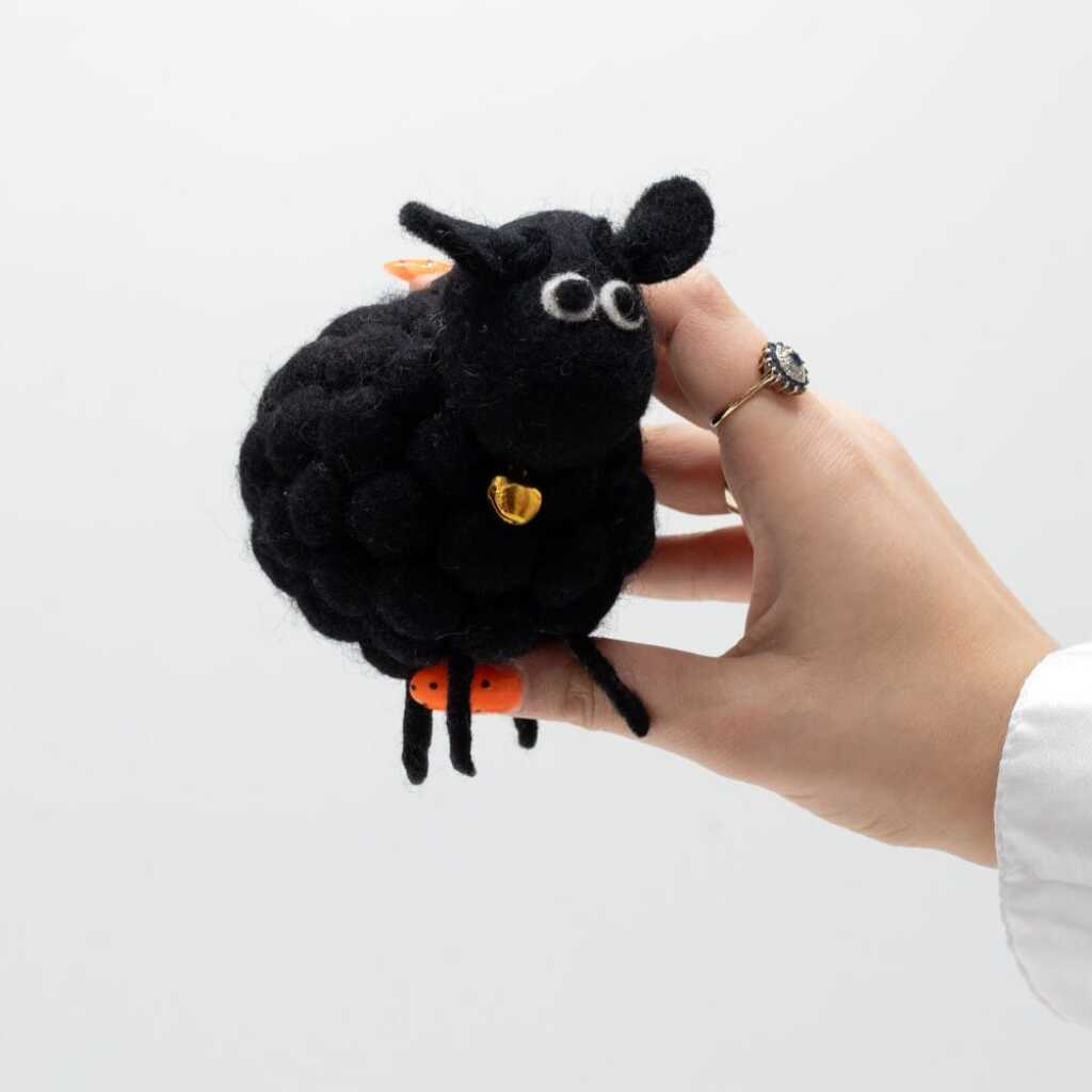 a little felt sheeps in black with a black head held in a hand