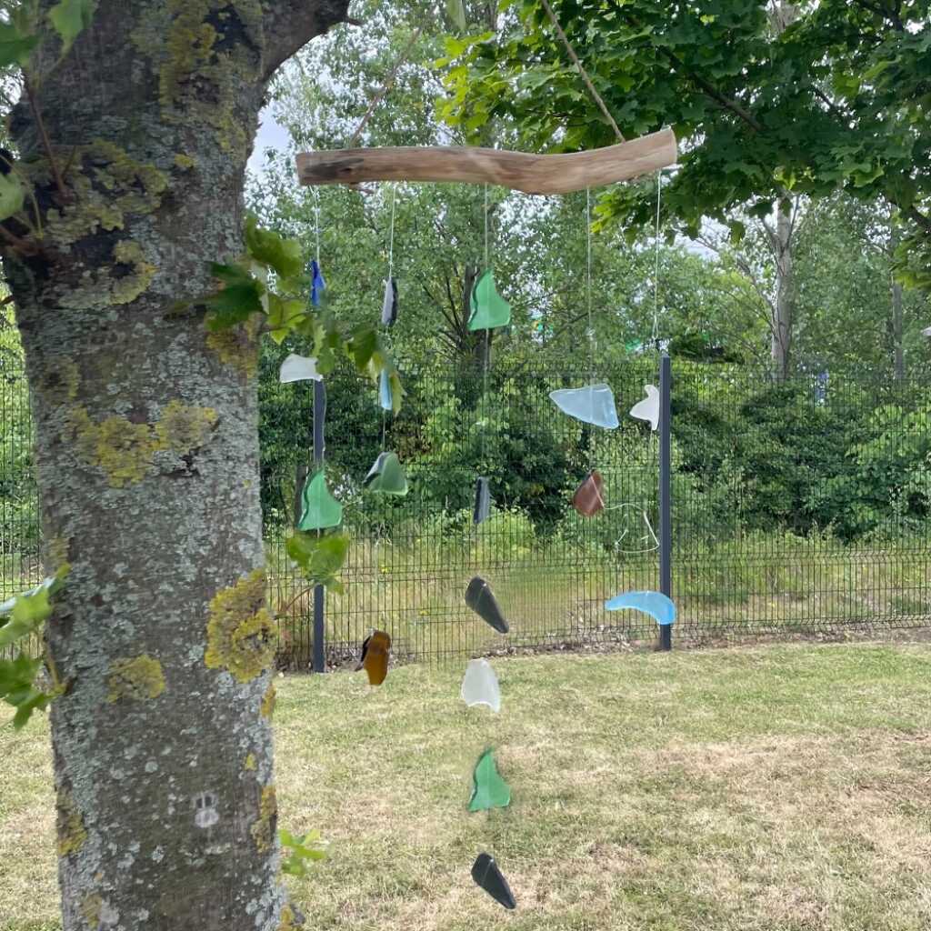 Driftwood and reclaimed glass wind chimes with five strings of beads., in a tree.