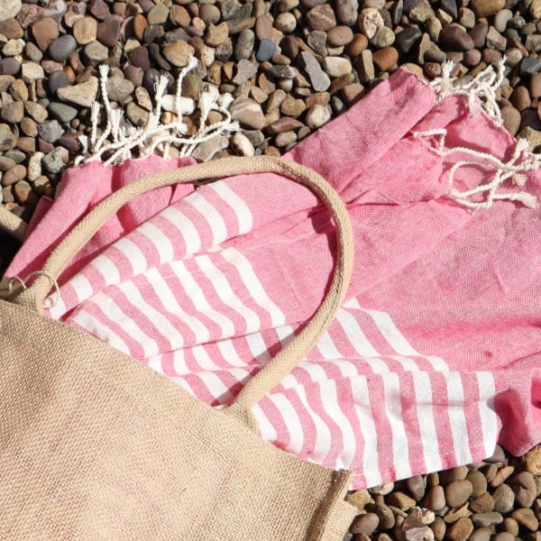 a pink and white cotton pareo throw in a beach bag