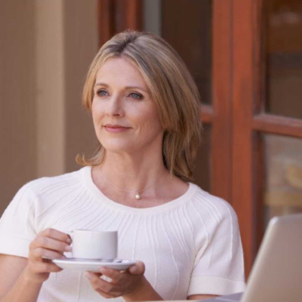 a lady in a white tee shirt drinking tea in front of a laptop