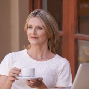 a lady in a white tee shirt drinking tea in front of a laptop